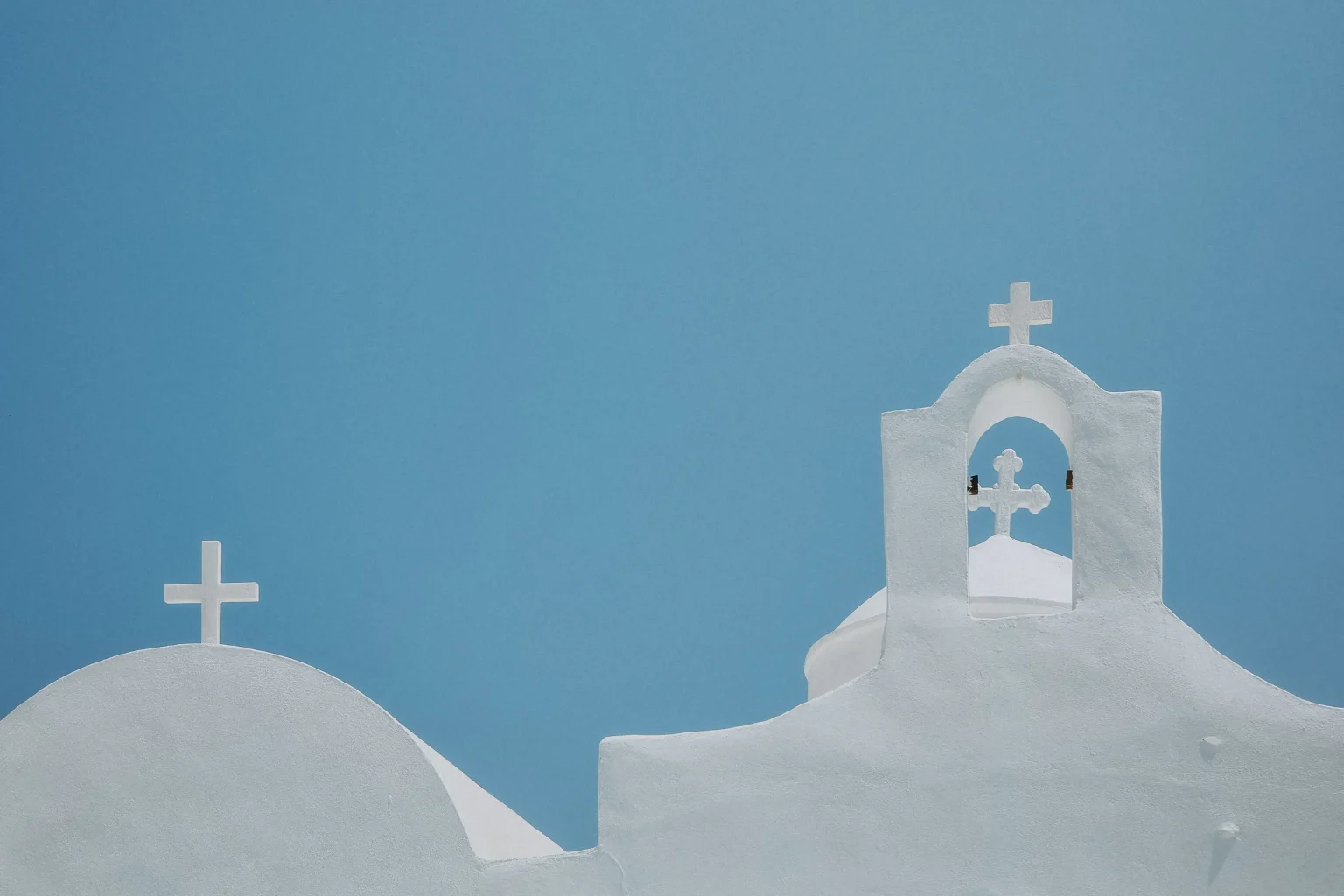 White domes, crosses and bell tower of Timios Stavros monastery against a clear blue sky in Sifnos