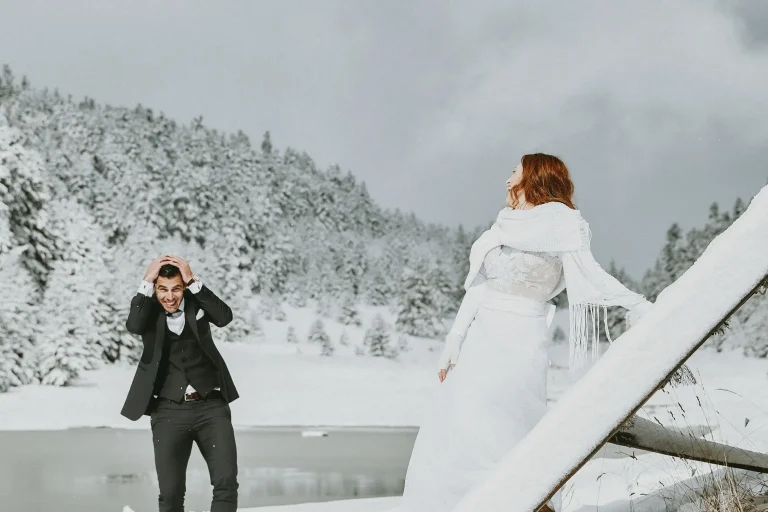 Elena laughing beside a snowy railing as Vassilis playfully holds his head during their day-after session