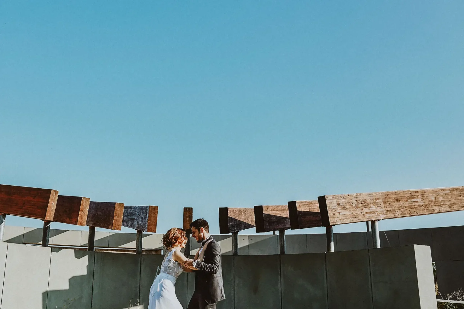 Elena and Vassilis facing each other beneath wooden beams and a clear blue sky after their winter wedding in Tatoi