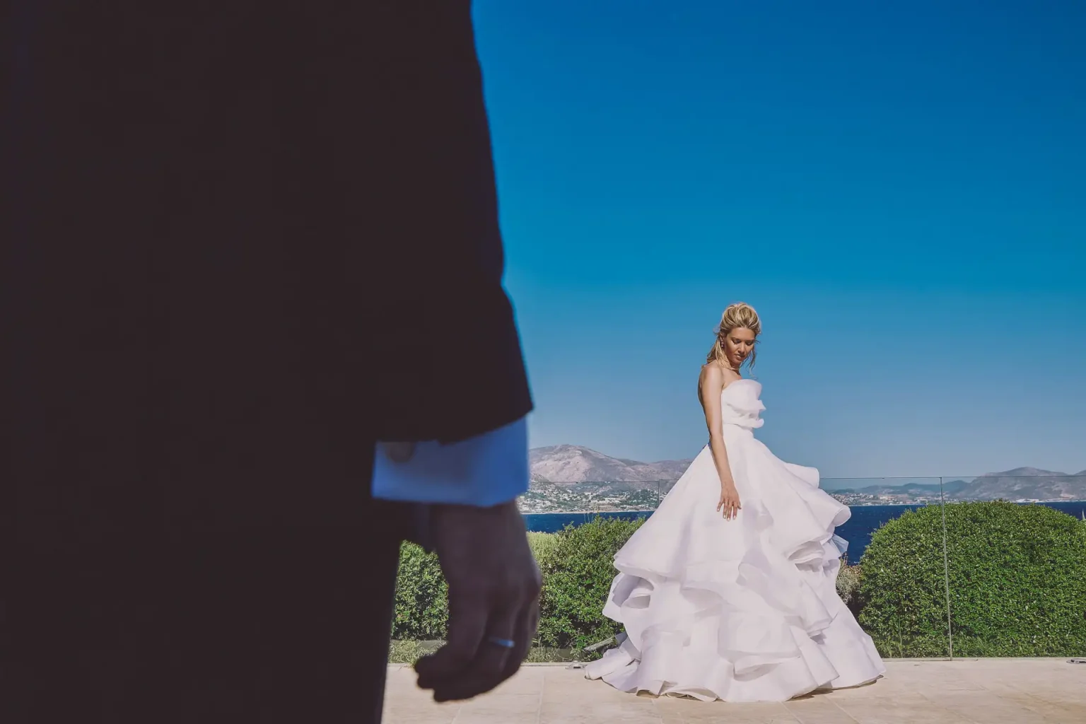 Anthi in her flowing wedding gown at Island Residence on the Athens Riviera, with the groom in the foreground