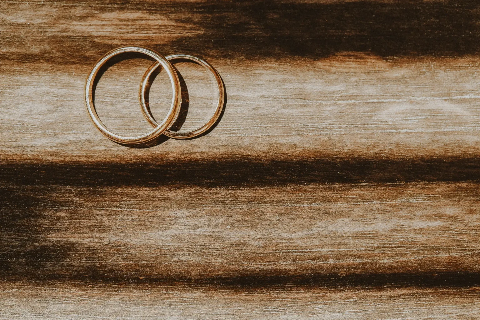 Two overlapping wedding rings on a wooden surface in warm sunlight