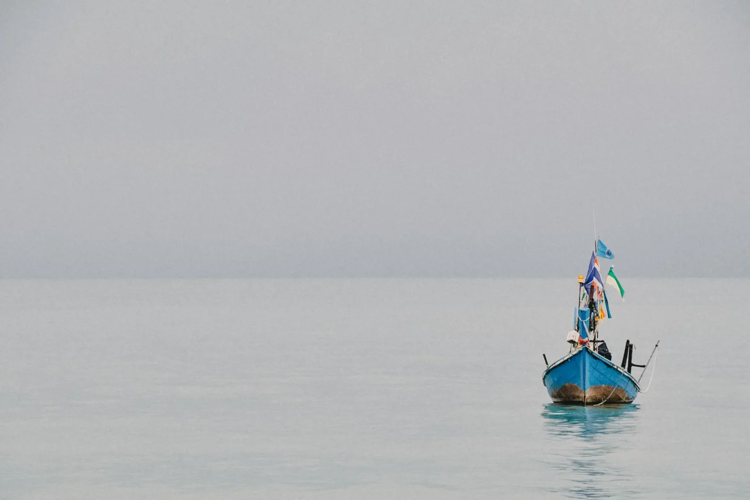 Blue fishing boat on calm water beneath an overcast sky in Koh Samui