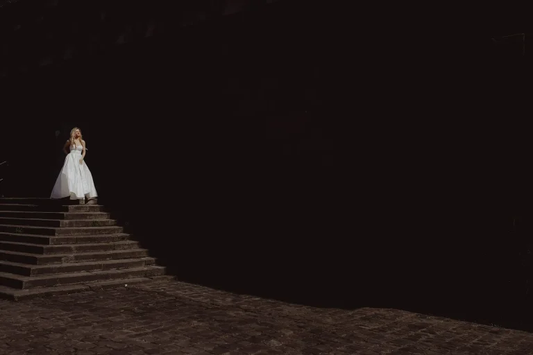 Minimal night portrait of Elena in her wedding dress standing on illuminated steps surrounded by darkness