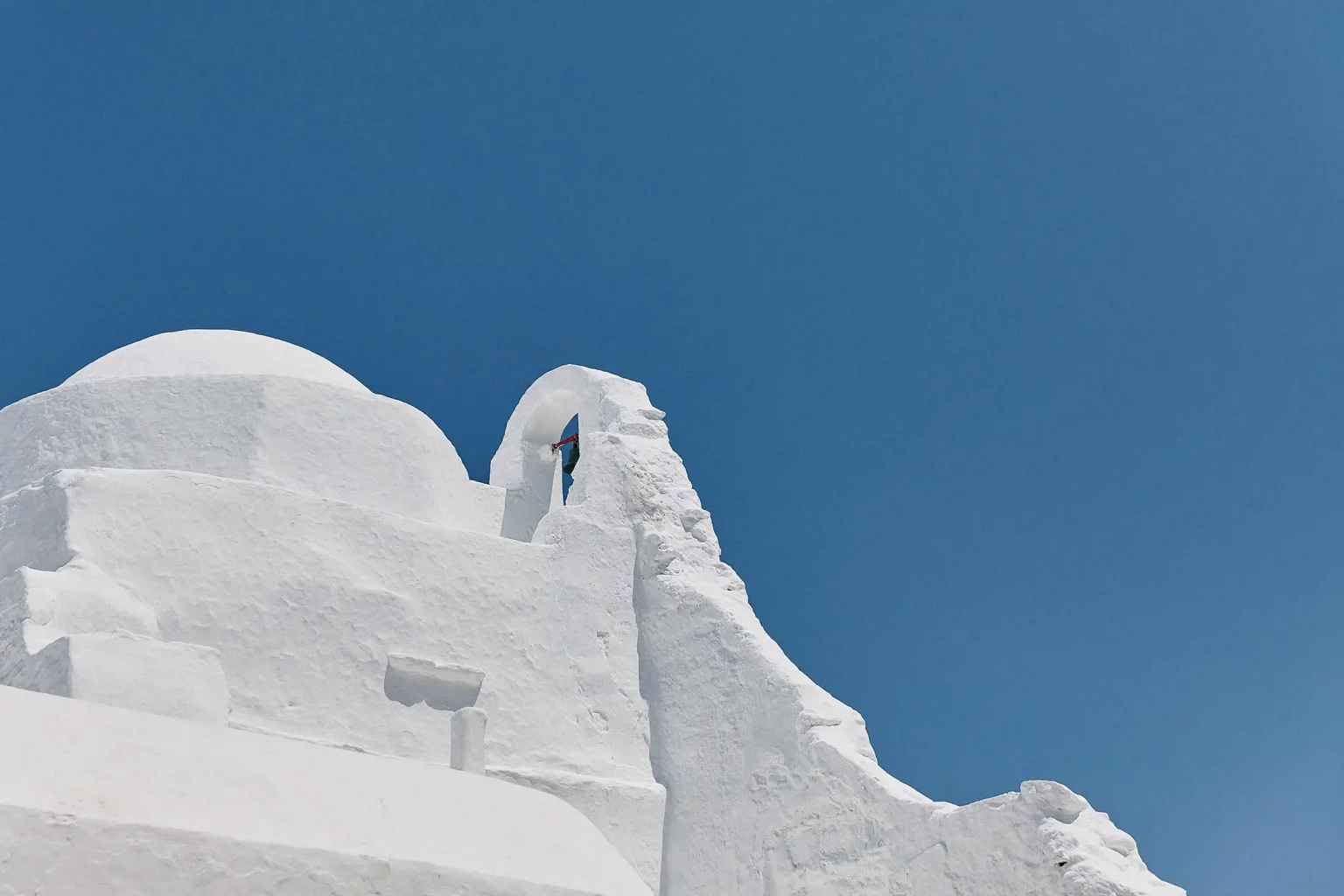 Whitewashed Paraportiani church and its bell tower beneath a clear blue sky in Mykonos