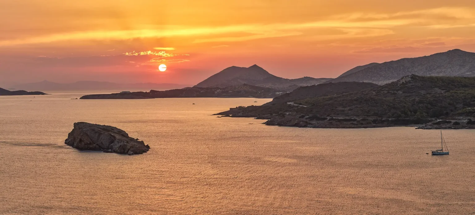 Golden sunset over the Athens Riviera, with rocky headlands and sailboats on the calm sea