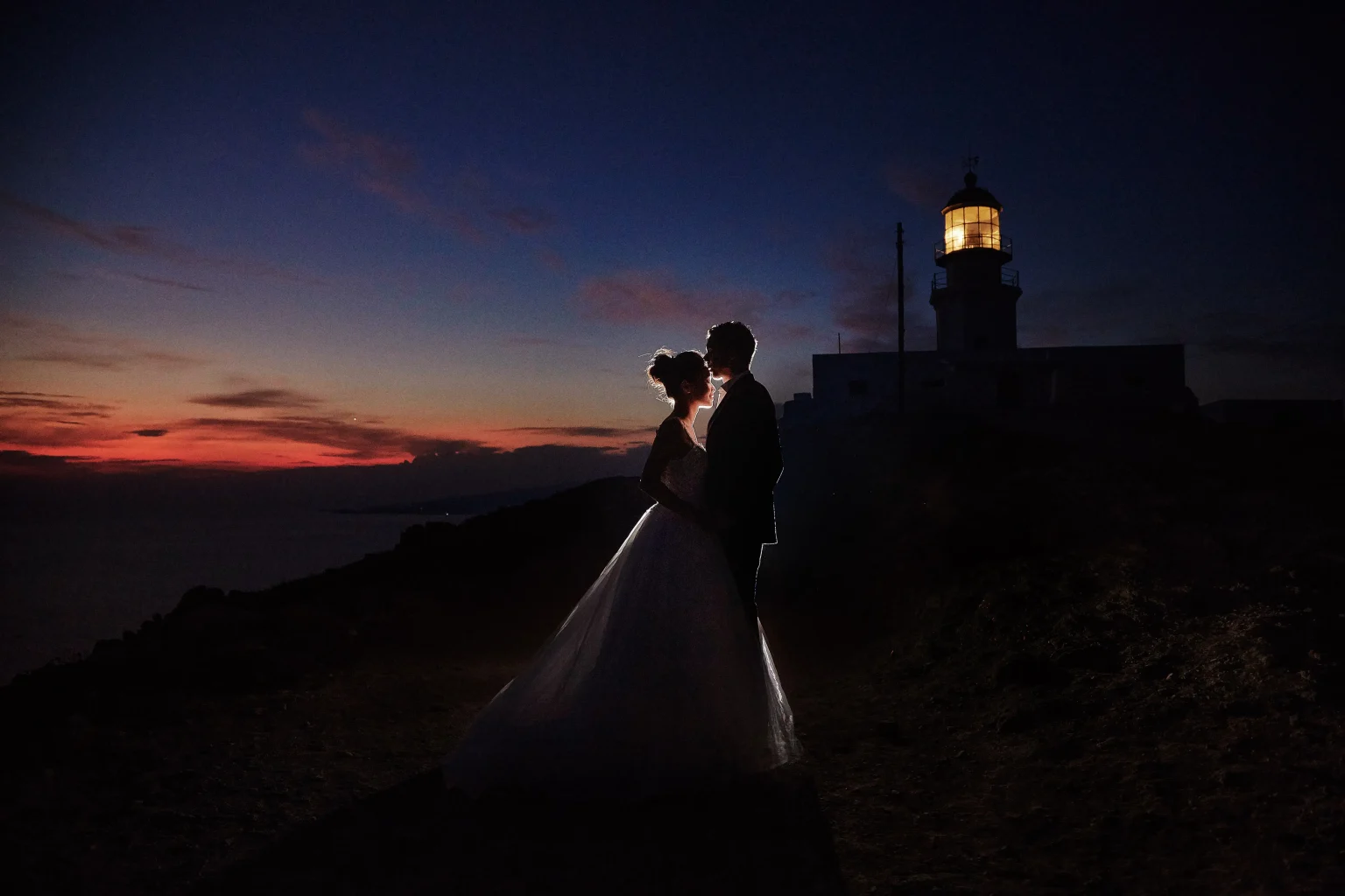 mykonos elopement photo of couple lighthouse after sunset with warm colours in the sky
