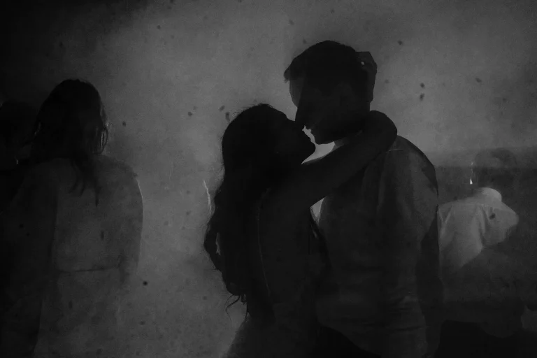Black-and-white silhouettes of Vas and Sebastian kissing amid confetti during their wedding reception.