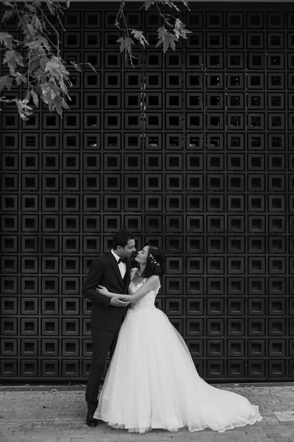 Black-and-white elopement portrait of Sandra and Romain embracing against a tall geometric wooden doorway in Athens.