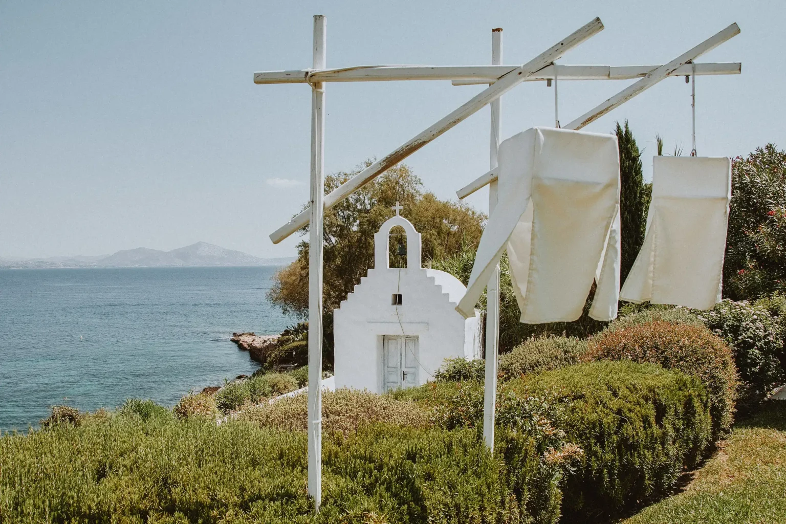 Agios Dionysios chapel overlooking the sea at Island Gallery, with white fabric hanging from wooden frames